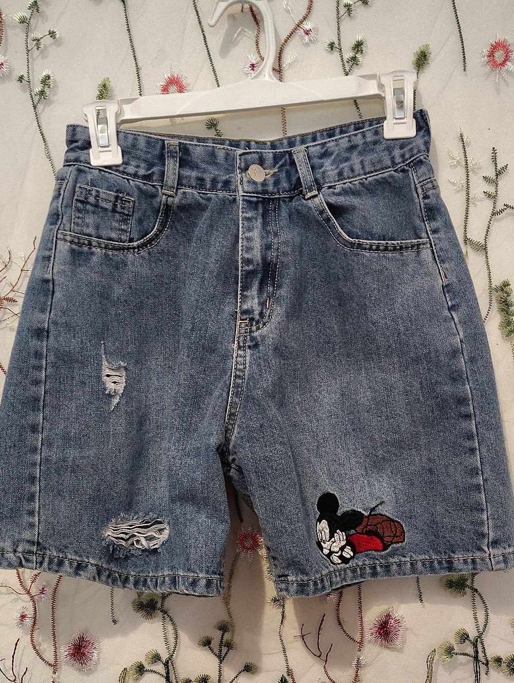 medium-wash denim shorts feature an embroidered Mickey Mouse patch